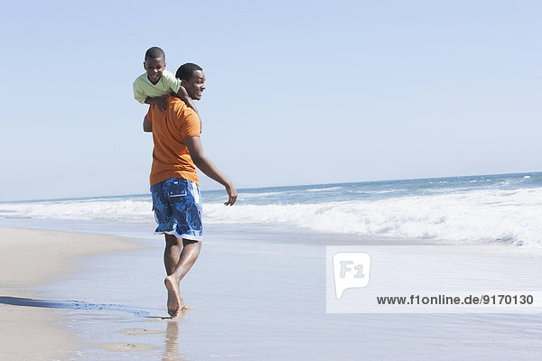 Father carrying son in waves on beach