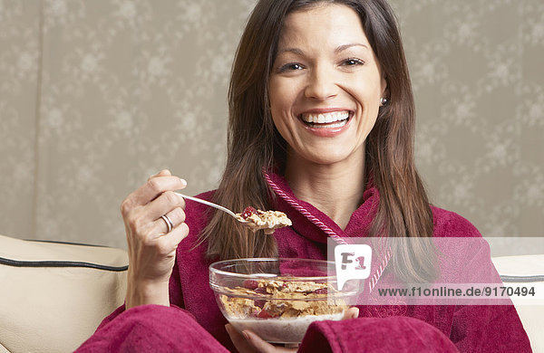 Mixed race woman eating cereal on sofa