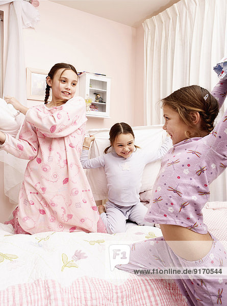 Mixed race girls having pillow fight on bed