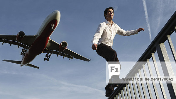 Deutschland,  Mittlerer Erwachsener Mann mit Flugzeug im Hintergrund blanchierend auf Geländer