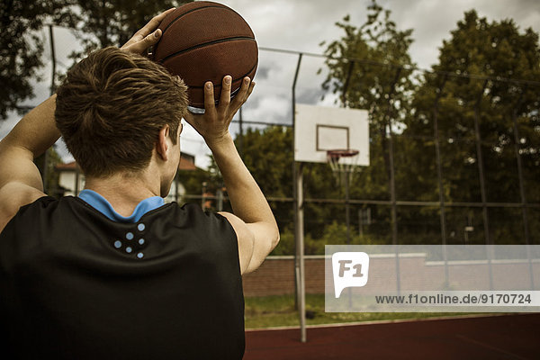 Junger Basketballspieler auf Basketballkorb  Rückansicht