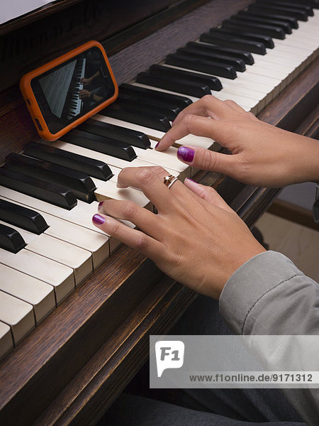 Young woman playing piano with the assistance of smartphone  partial view