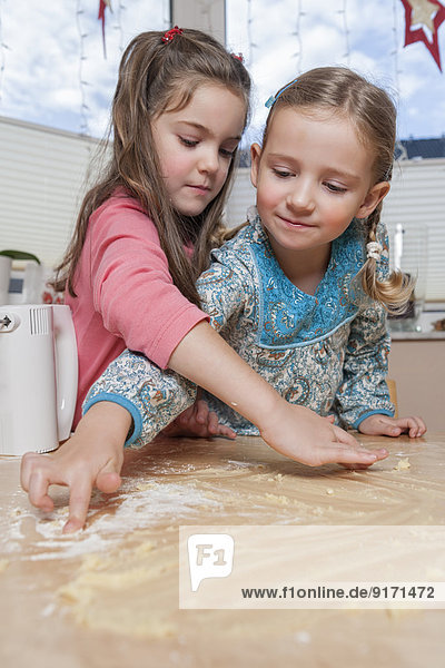 Porträt von zwei kleinen Mädchen mit Teigresten auf dem Küchentisch