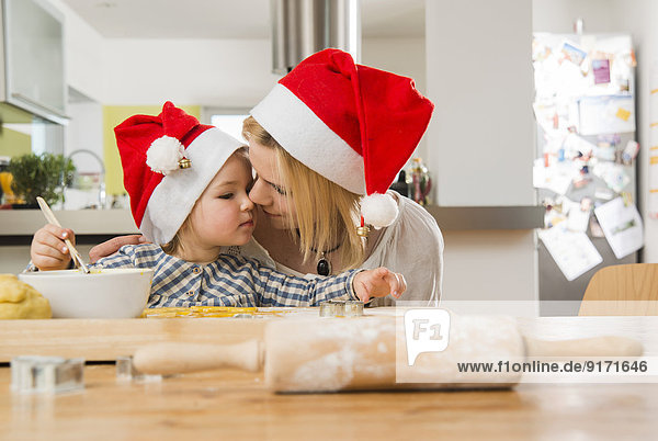 Mutter und Tochter mit Weihnachtsmützen beim Backen in der Küche