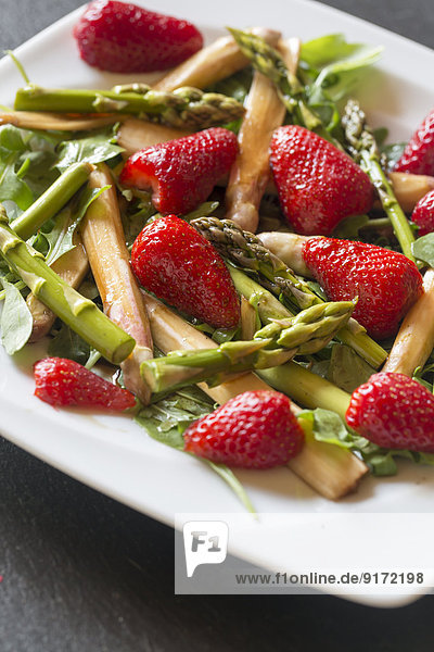 Dish with salad of green and white asparagus  rocket salad and strawberries