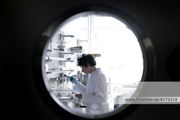 Chemikerin bei der Arbeit im Labor beobachtet durch Spionageloch