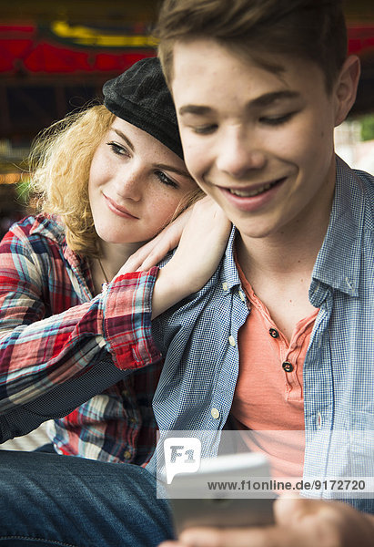 Portrait of teenage couple using smartphone at fun fair