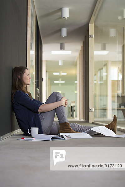 Porträt einer Geschäftsfrau  die auf dem Boden im Flur des Büros sitzt.