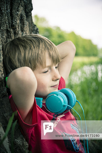 Porträt eines entspannenden Jungen mit Kopfhörer auf Baum gelehnt
