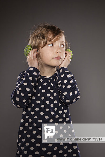 Portrait of little girl holding broccoli on his ears