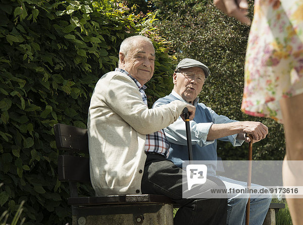 Zwei alte Männer sitzen auf der Parkbank und beobachten die Beine der vorbeifahrenden Frau.