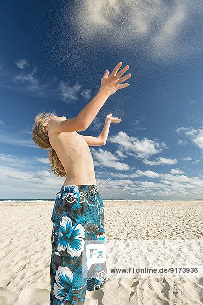 Australien  New South Wales  Pottsville  Junge am Strand wirft Sand in die Luft