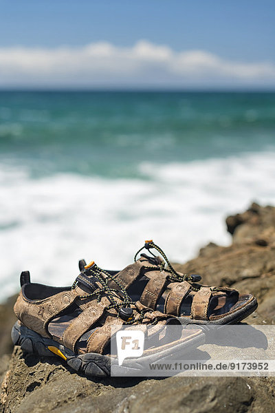 Australia  New South Wales  Byron Bay  Broken Head nature reserve  trekking sandals on rocks with breaking waves behind