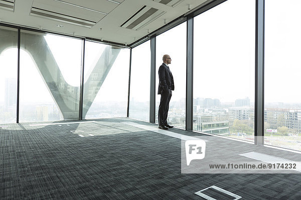 Businessman on empty office floor looking out of window