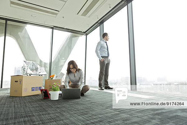 Businesswoman using laptop on empty office floor with cardboard boxes