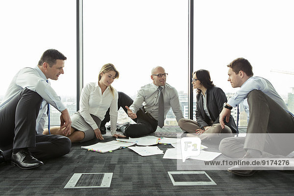 Geschäftsleute  die auf dem Boden sitzen und über Papiere diskutieren.