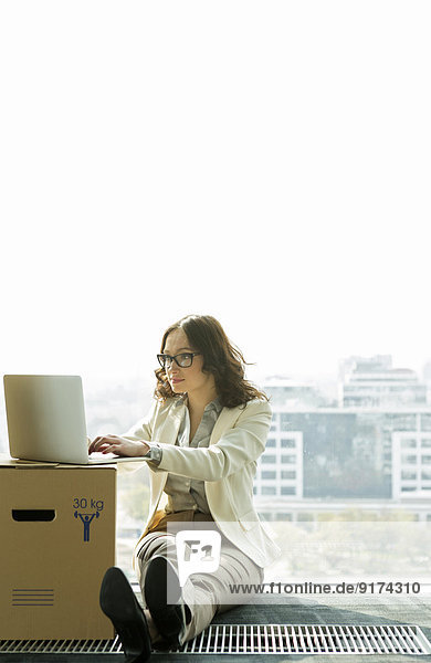 Geschäftsfrau mit Laptop auf leerer Büroetage mit Pappkartons