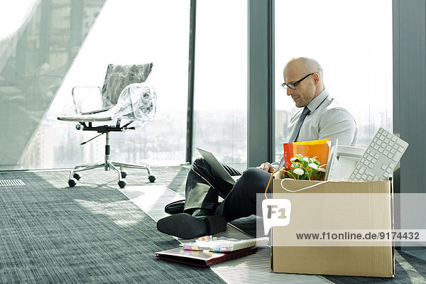 Businessman using laptop on empty office floor with cardboard box