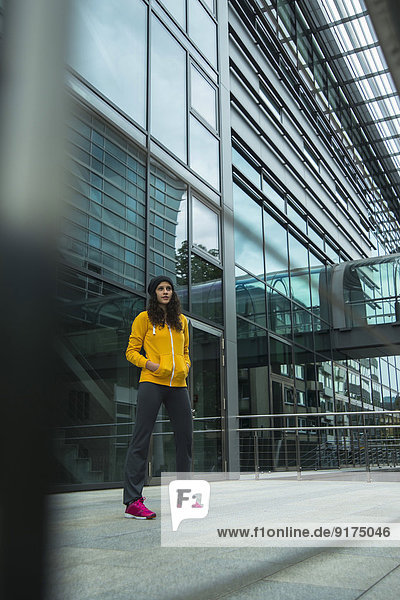 Junge Frau im gelben Trainingsanzug Top vor Glasfront stehend