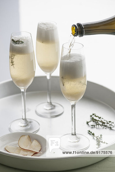 Tablett mit drei Champagnerflöten aus Champagner mit Birnenpurree und Thymian