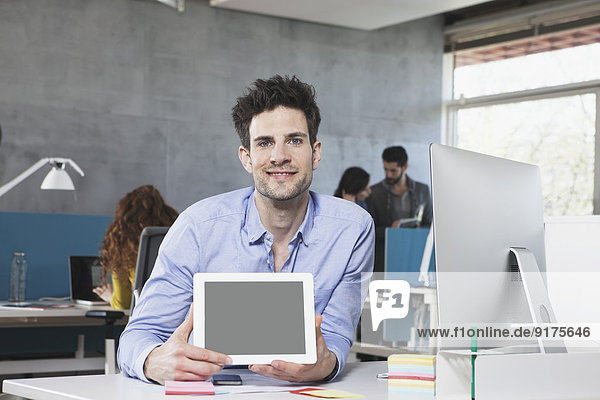 Portrait of smiling man showing tablet computer in the office