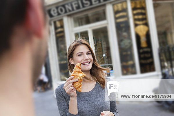 France  Paris  portrait of young woman showing croissant in front of pastry shop