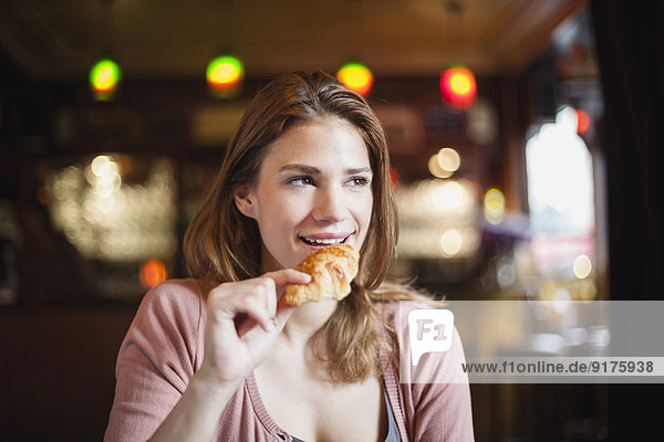 Frankreich  Paris  Porträt einer glücklichen jungen Frau  die ein Croissant in einem Café isst.