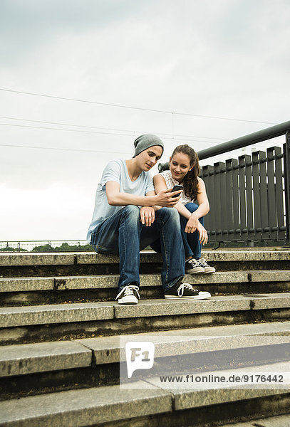 Junges Paar mit Smartphone auf der Treppe sitzend