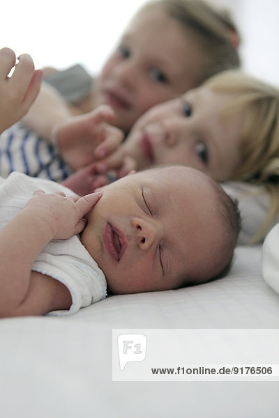 Portrait of newborn baby boy and his two sisters in the background