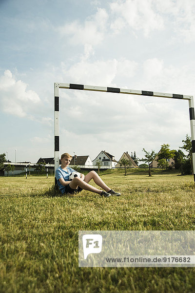 Germany  Mannheim  Teenage boy sitting on grass  leaning on goal