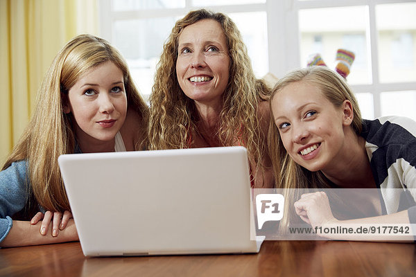 Mother and her two daughters lying on wooden floor at home using laptop