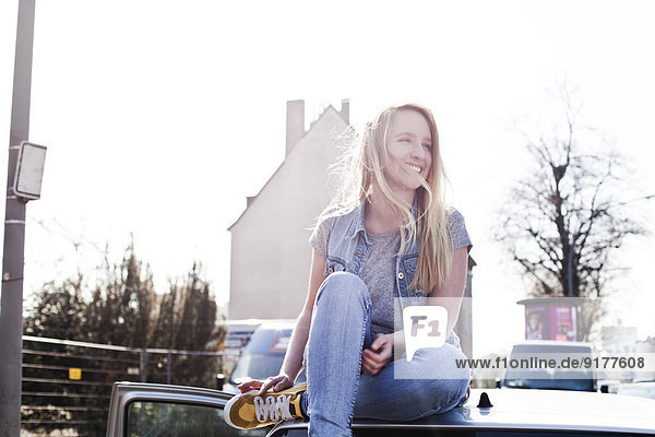 Lächelnde junge Frau auf dem Autodach sitzend