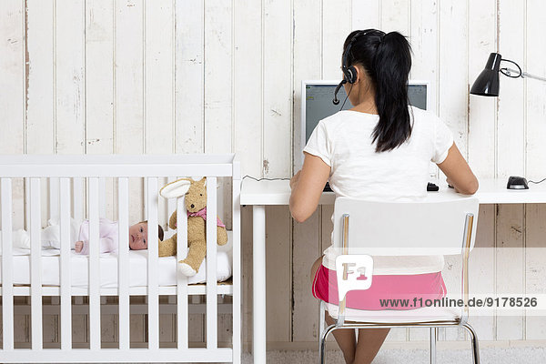 Frau arbeitet im Home Office  während ihr Baby im Kinderbett liegt.
