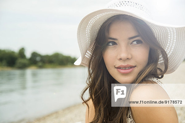 Porträt einer jungen Frau am Strand mit weißem Sommerhut