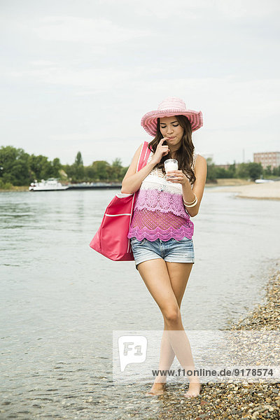 Junge Frau mit Hut und Tasche am Rheinufer stehend