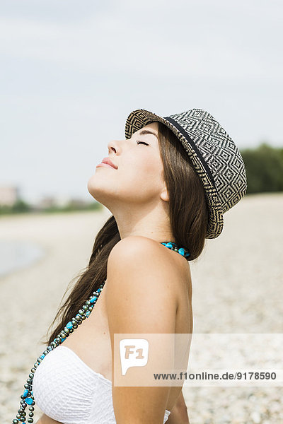 Porträt einer jungen Frau mit Hut  die sich am Strand entspannt