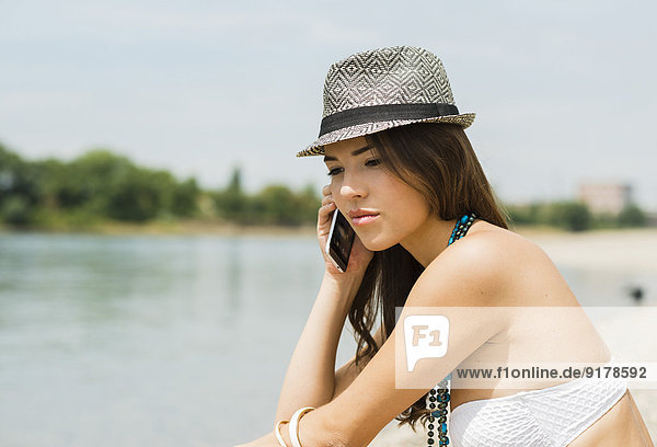 Portrait einer jungen Frau beim Telefonieren am Strand