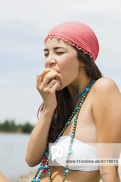 Porträt einer jungen Frau beim Essen eines Apfels am Strand