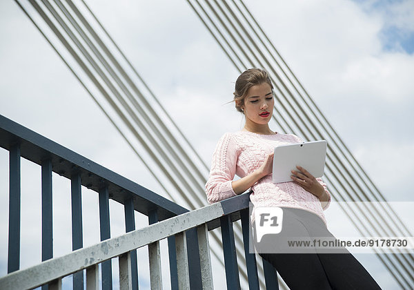Junge Frau auf dem Geländer mit digitalem Tablett
