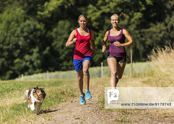 Zwei junge Frauen joggen mit Hund auf dem Feldweg