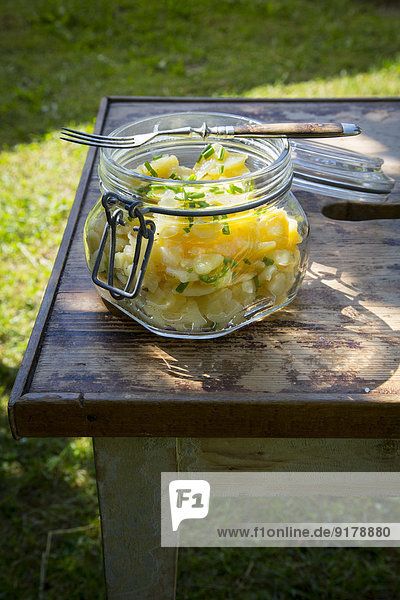Einmachglas mit schwäbischem Kartoffelsalat und Gabel auf Holztisch im Garten