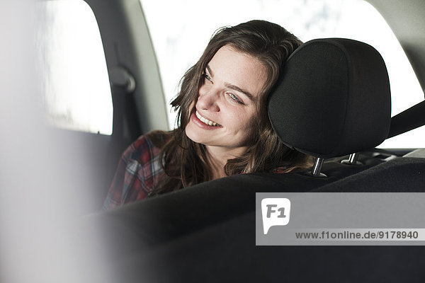 Lächelnde junge Frau auf dem Rücksitz eines Autos