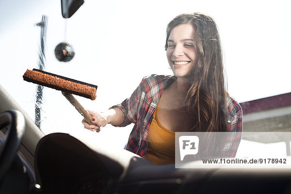 Lächelnde junge Frau reinigt Windschutzscheibe eines Autos