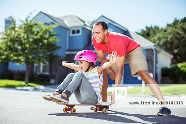 Vater schiebt Tochter auf Skateboard