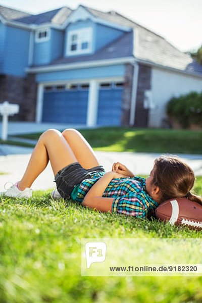 Mädchen liegt auf Fußball im Rasen vor dem Haus