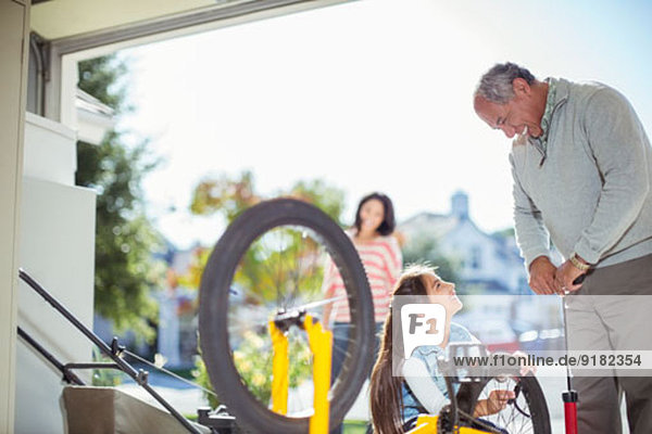 Großvater und Enkelin beim Aufpumpen von Fahrradreifen in der Garage