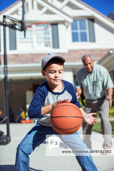 Großvater und Enkel beim Basketballspielen in der Einfahrt