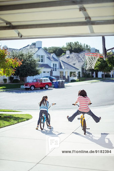 Girls riding bicycles in sunny driveway