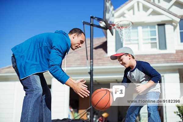 Vater und Sohn spielen Basketball in sonniger Einfahrt