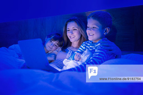 Mutter und Kinder mit digitalem Tablett im Bett